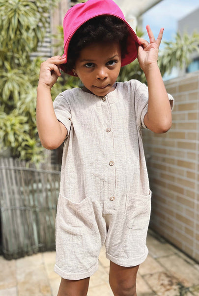 Menina com macacão curto cor Cru e chapéu bucket - Loja com macacão jardineira macaquinho unissex  para infantil online